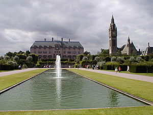 A rectangular lake with a central fountain, beyond which is the house, with the clock tower and chapel to its right